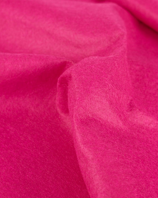 A close up of bright pink draped wool and viscose felt fabric, gathered to show its firm structure and texture. 