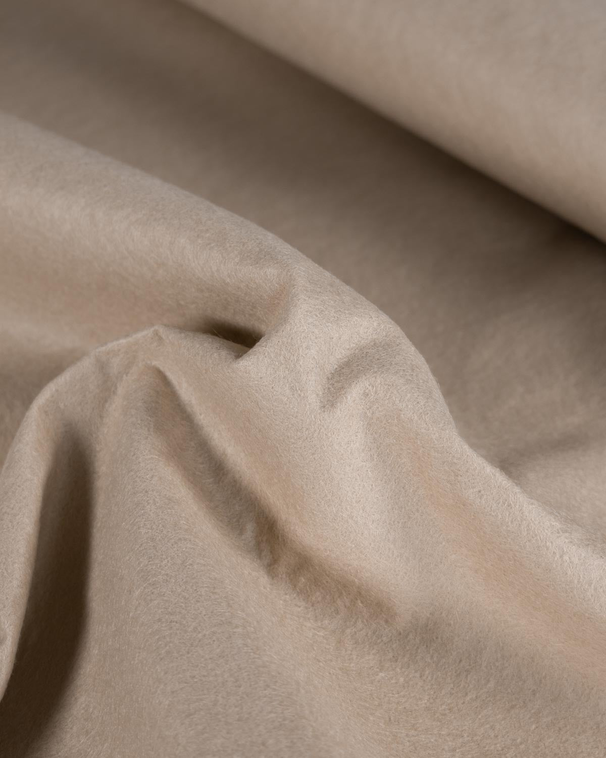 A close-up of draped beige light stone wool and viscose felt fabric with soft folds and a smooth, matte texture.
