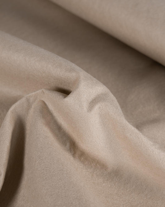 A close-up of draped beige light stone wool and viscose felt fabric with soft folds and a smooth, matte texture.