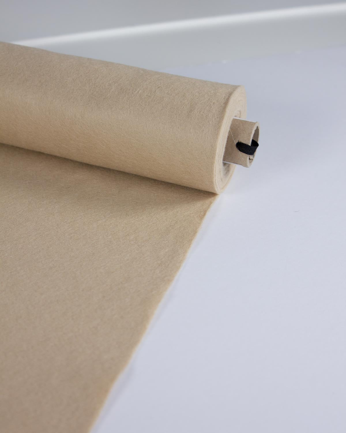 A roll of light stone beige wool and viscose felt fabric unrolled onto a clean white surface.