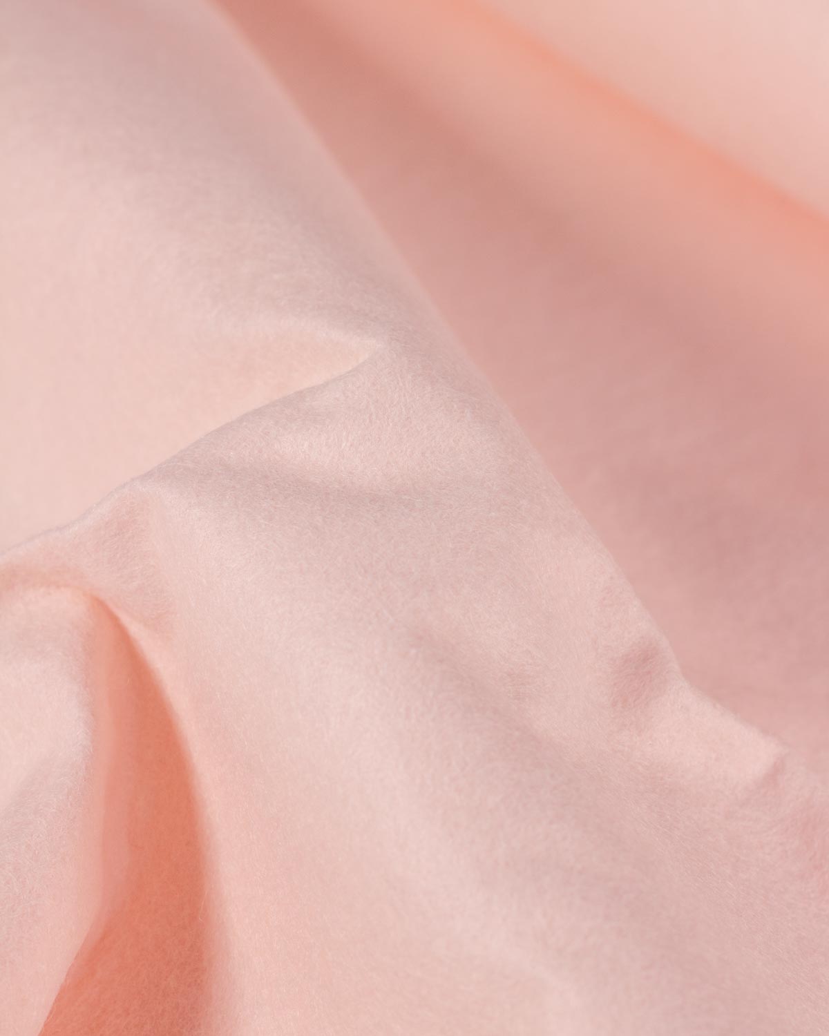 A gathered piece of flesh pink coloured wool and viscose felt fabric, showing off its firm structure and textured surface. 