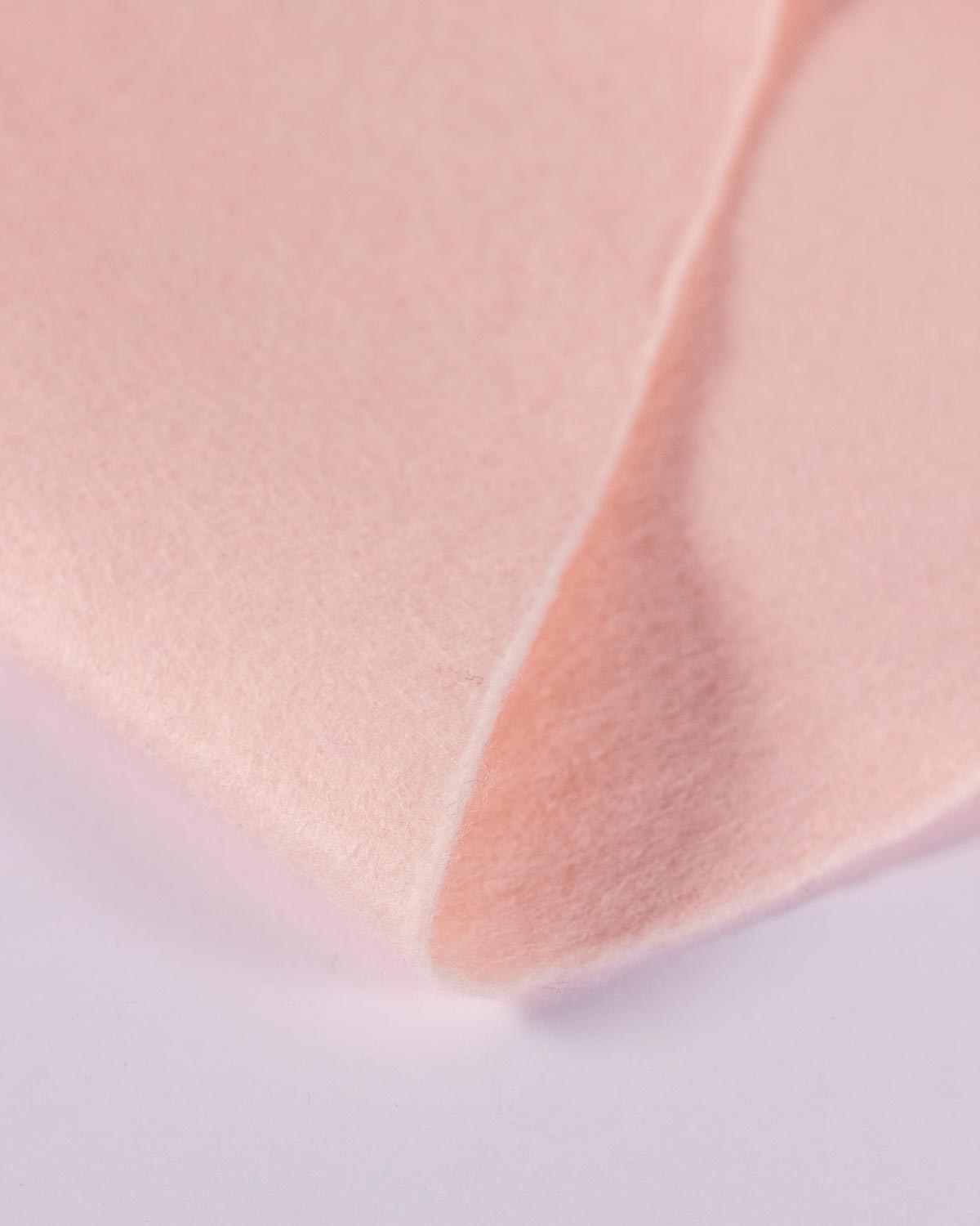 A piece of flesh pink wool and viscose felt fabric folded on a white background, showing its light colour and textured surface. 