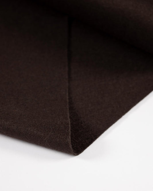 A close-up of dark brown wool and viscose felt fabric folded over on a white background, showing its soft, matte texture.