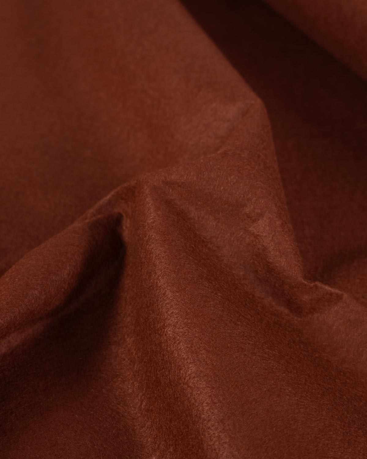 A piece of chestnut brown wool and viscose felt fabric, gathered up to show its firm structure and texture.
