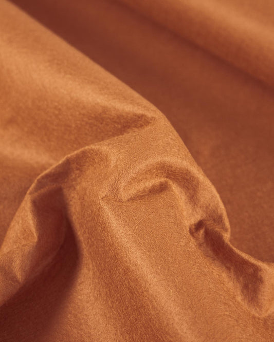 A close-up of draped ginger brown wool and viscose felt fabric with soft folds and a matte texture.