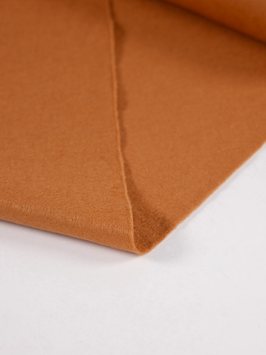 A close-up of folded ginger brown wool and viscose felt fabric showing its soft texture and color on a clean white background.