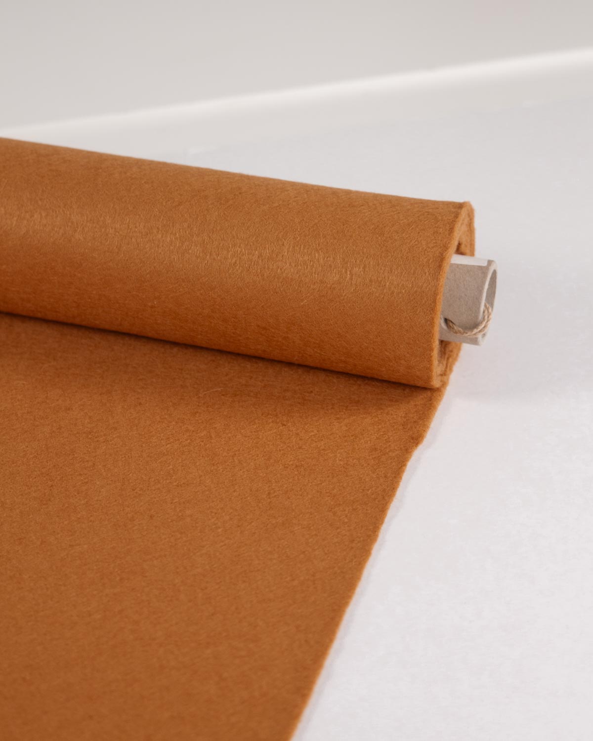 A roll of warm ginger brown wool and viscose felt fabric, partially unrolled on a clean white surface.