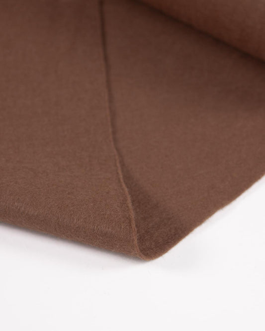 A piece of light brown folded wool and viscose felt fabric on a white surface, showing its texture and even colour.