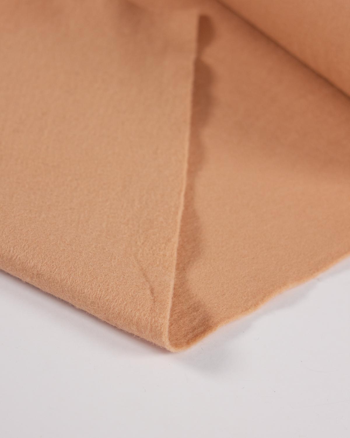 A piece of beige wool and viscose felt fabric folded on a white surface, showing its texture and even colour.