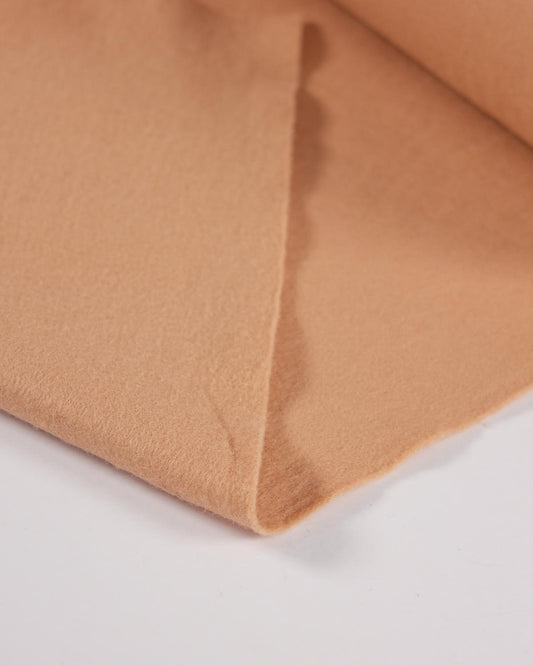A piece of beige wool and viscose felt fabric folded on a white surface, showing its texture and even colour.
