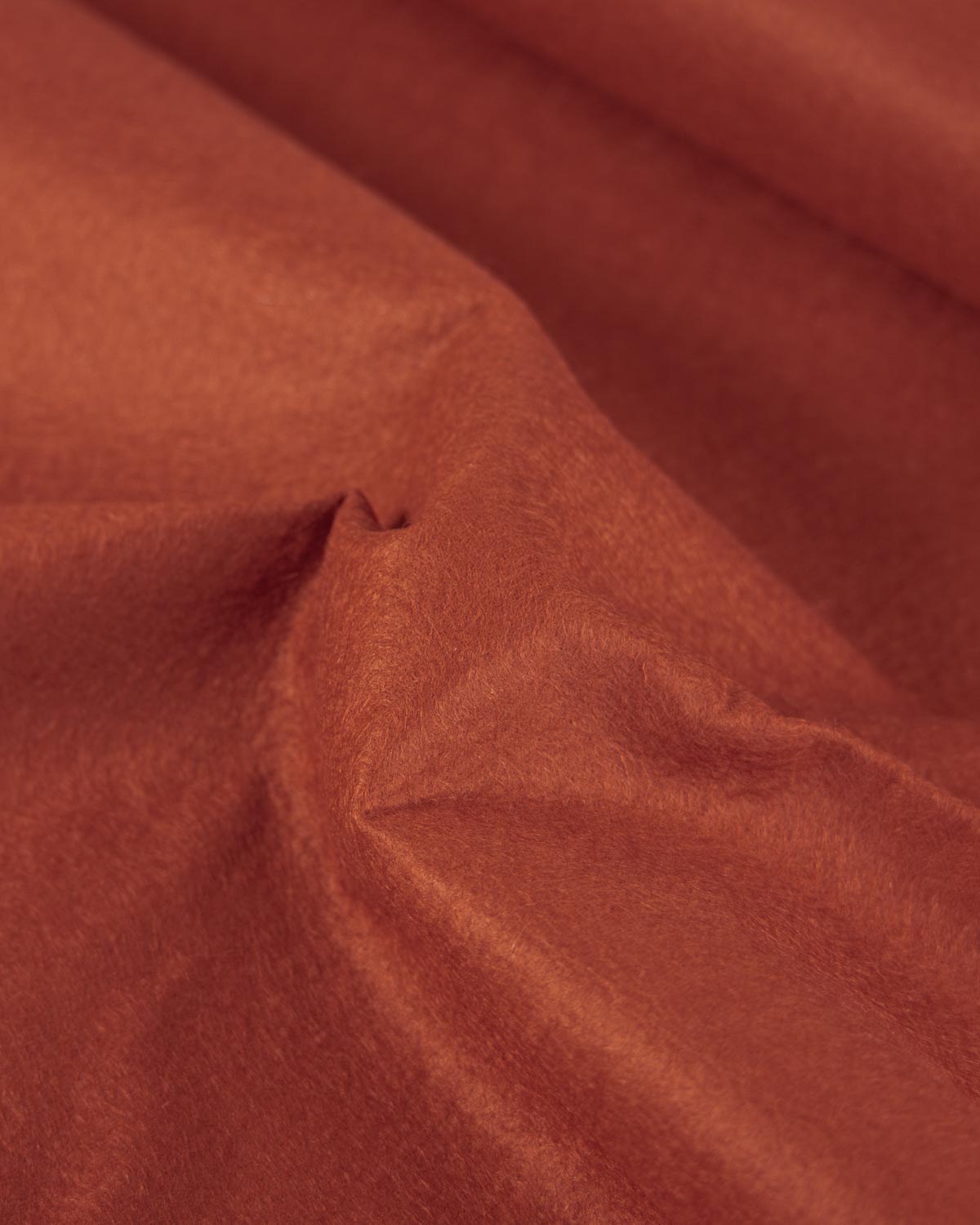 A close-up of draped terracotta colored wool and viscose felt fabric with a soft, slightly fuzzy texture.