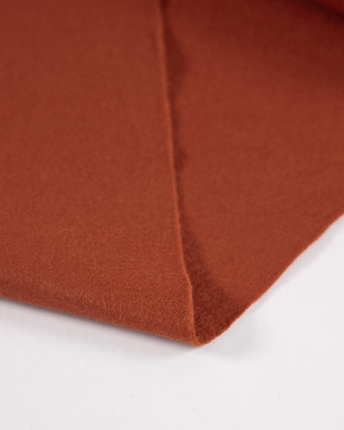 A piece of wool and viscose felt fabric folded on a white background, showing its texture and even colour. 