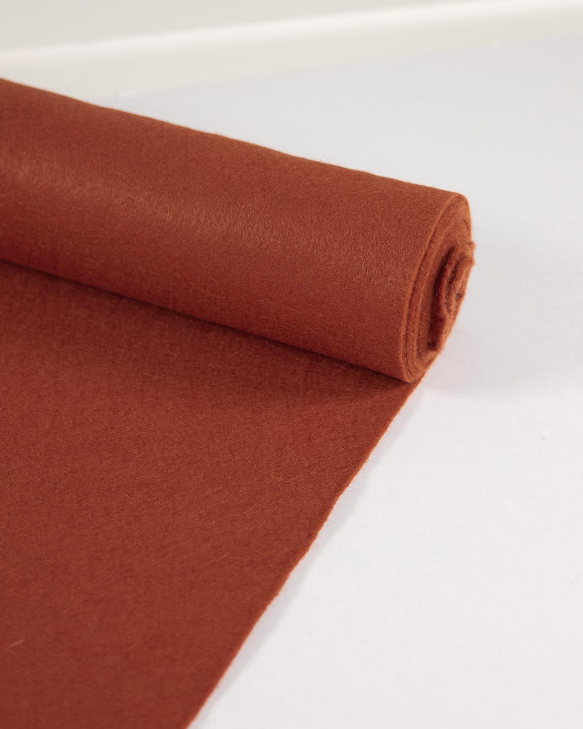 A roll of terracotta wool and viscose felt fabric partially unrolled on a clean white surface.