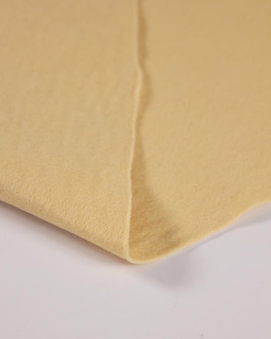 A close-up of a folded piece of soft, biscuit cream wool and viscose felt fabric on a plain white background.