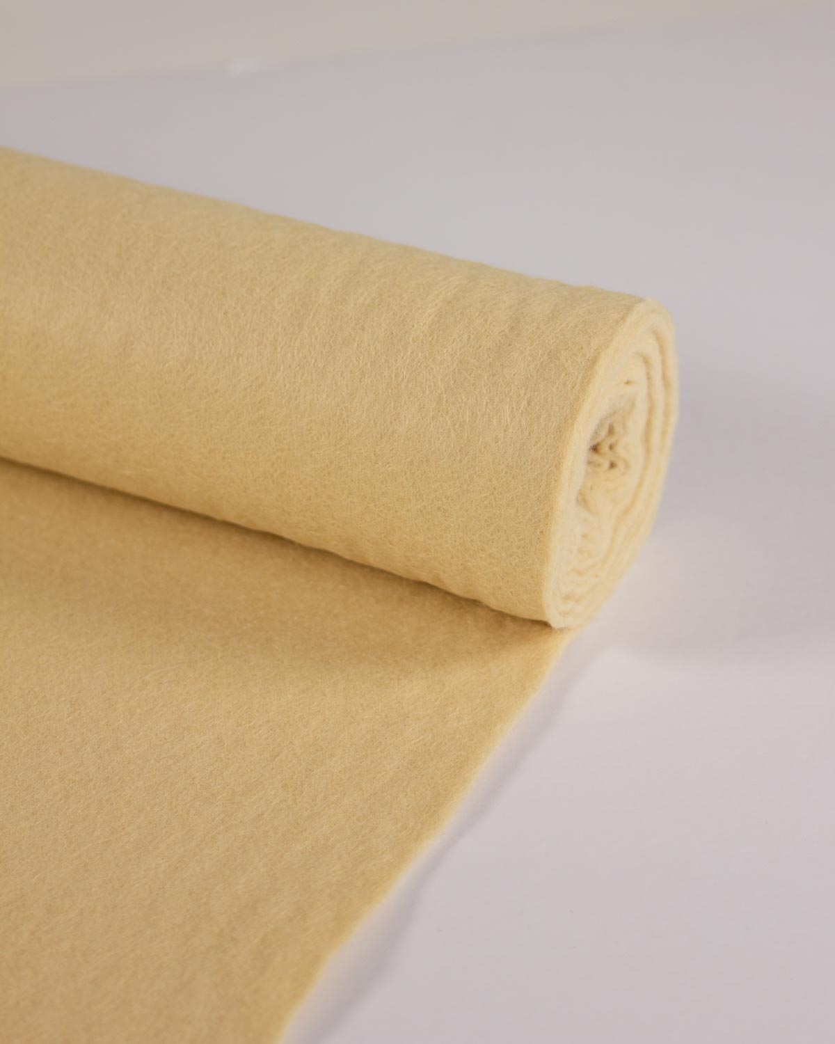 A roll of biscuit-cream wool and viscose felt fabric, partially unrolled to show its soft, matte texture on a clean white background.