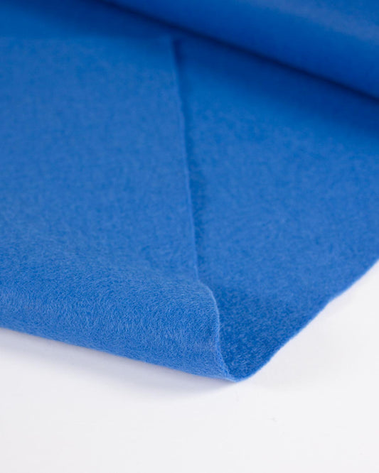 A close-up of a folded blue wool and viscose felt fabric showing its soft, textured surface on a clean white background.