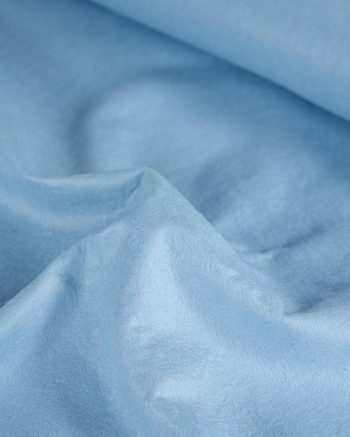 A close-up of light blue textured wool and viscose felt fabric with soft folds and a smooth matte finish.