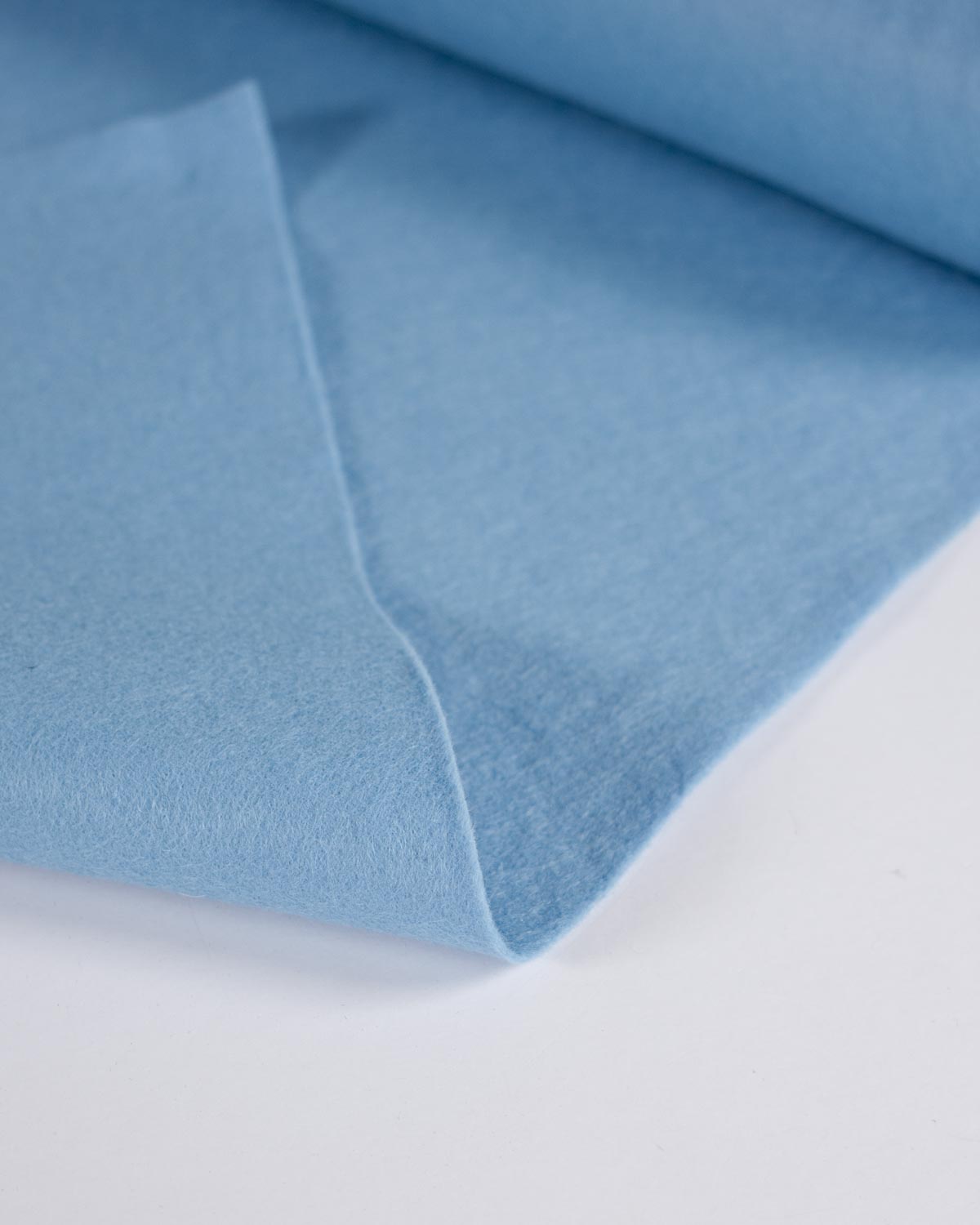 Light blue wool and viscose felt fabric folded over on a plain white surface, showing its soft, matte texture.