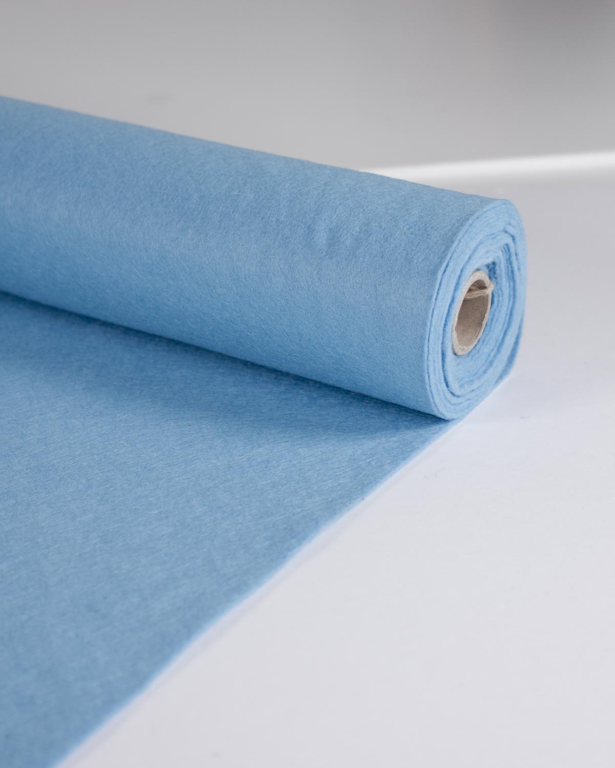 A roll of light blue wool and viscose felt fabric material unrolled slightly on a clean white surface.