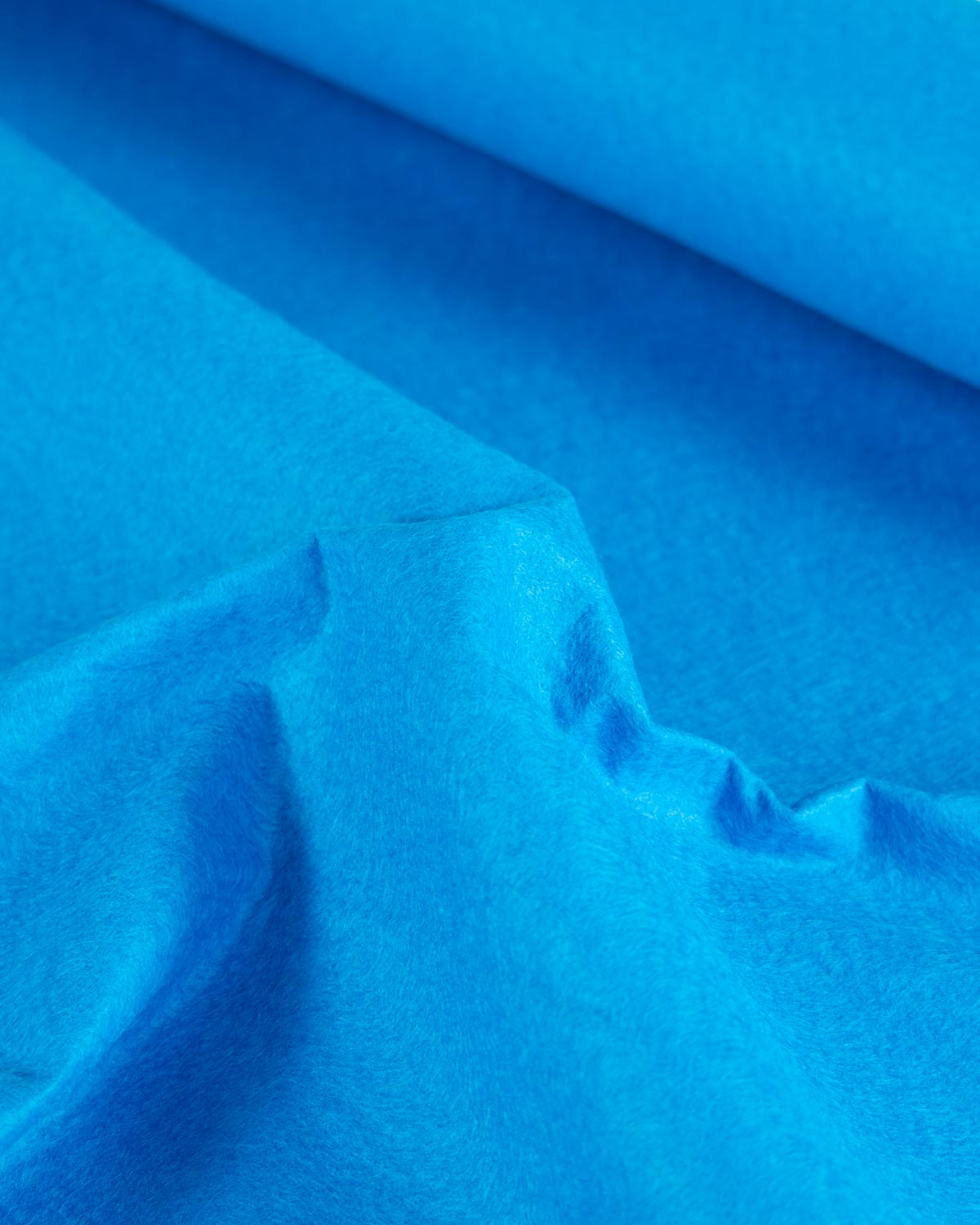 A piece of bright blue peacock wool and viscose felt fabric scrunched up to show its structure and texture. 