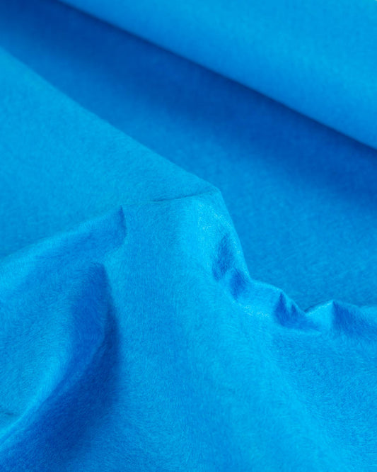 A piece of bright blue peacock wool and viscose felt fabric scrunched up to show its structure and texture. 