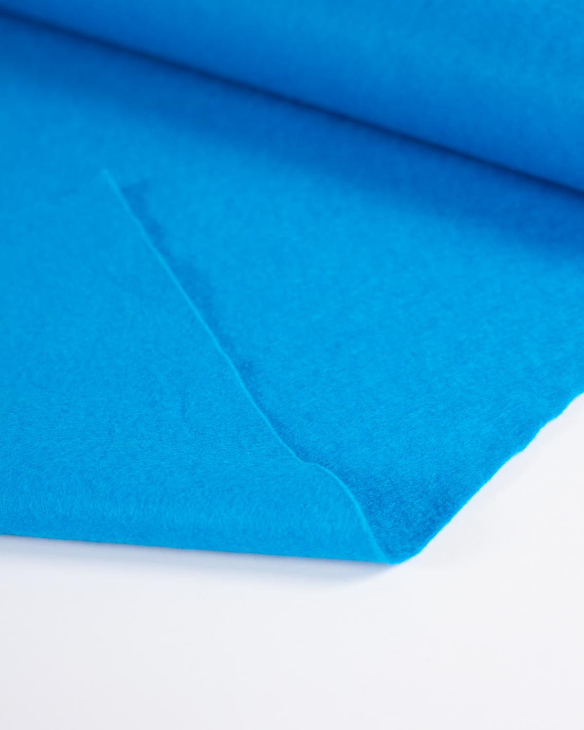 A piece of bright blue peacock wool and viscose felt fabric, folded to show its even matte surface on a white surface.