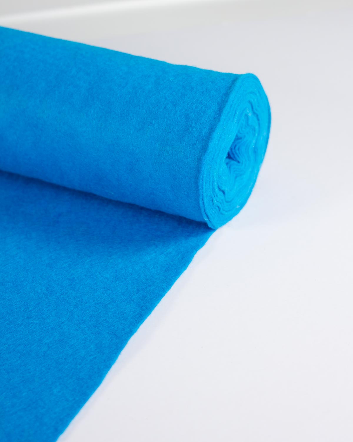 A bright blue roll of wool and viscose felt fabric material partially unrolled on a clean white surface.