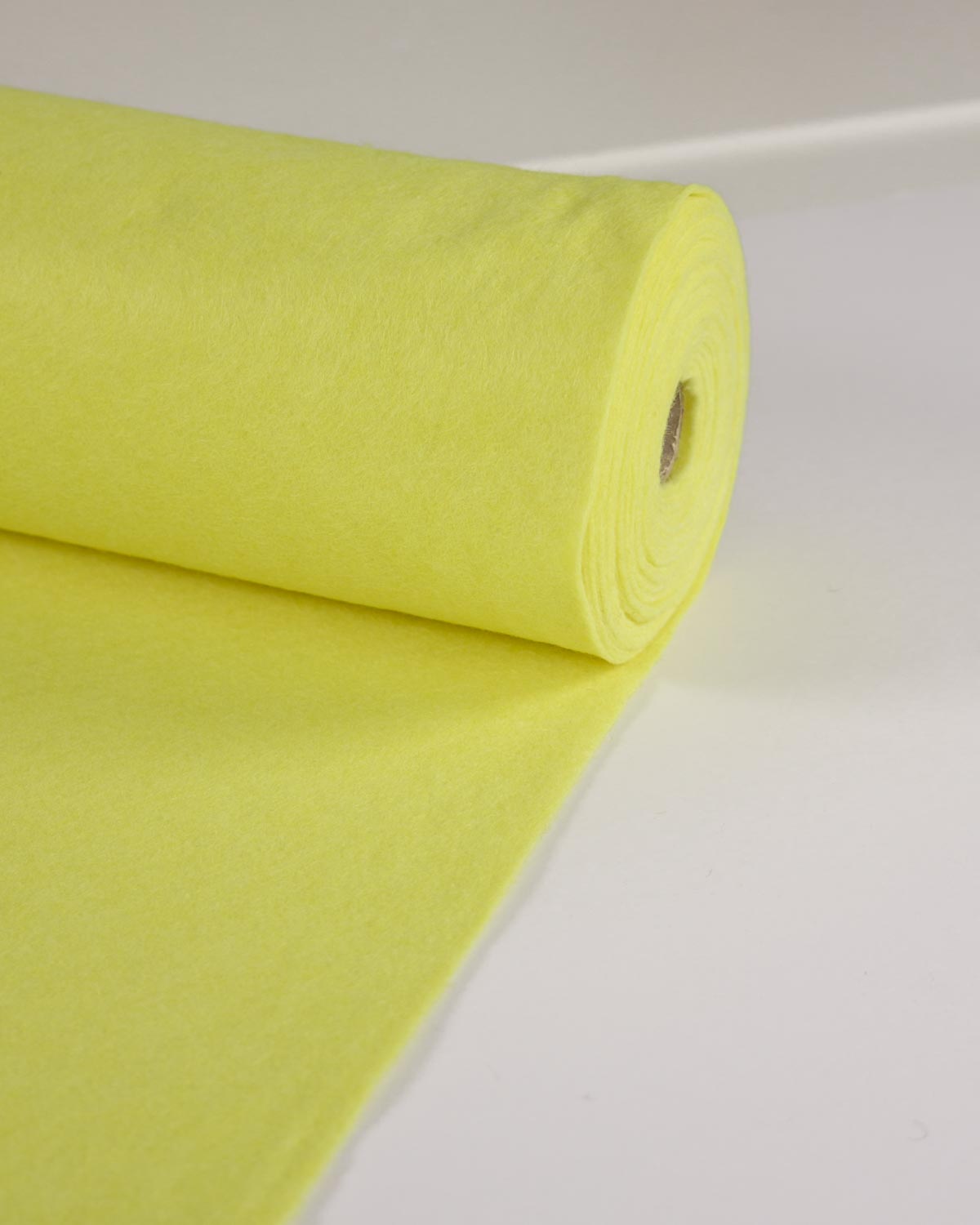 A roll of bright lemon-yellow wool and viscose felt fabric, unrolled onto a flat white surface.