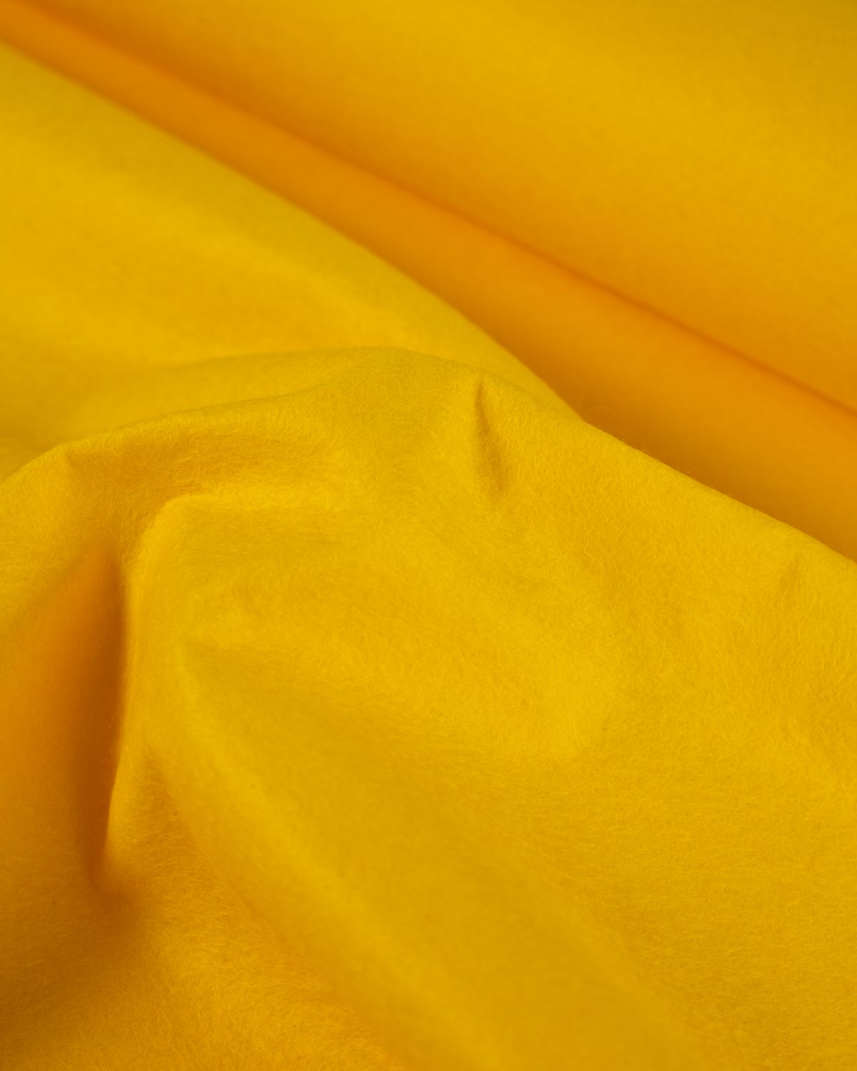 A close-up of draped warm yellow wool and viscose felt fabric with soft folds and a subtle sheen.