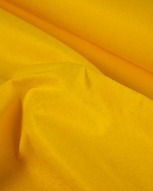 A close-up of draped warm yellow wool and viscose felt fabric with soft folds and a subtle sheen.
