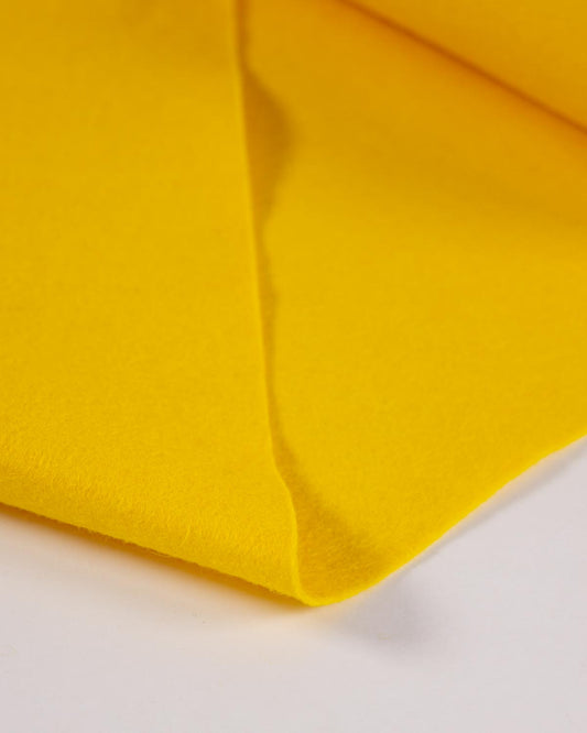 A folded piece of warm yellow wool and viscose felt fabric, folded on a white surface, showing its even, bold colour and texture. 