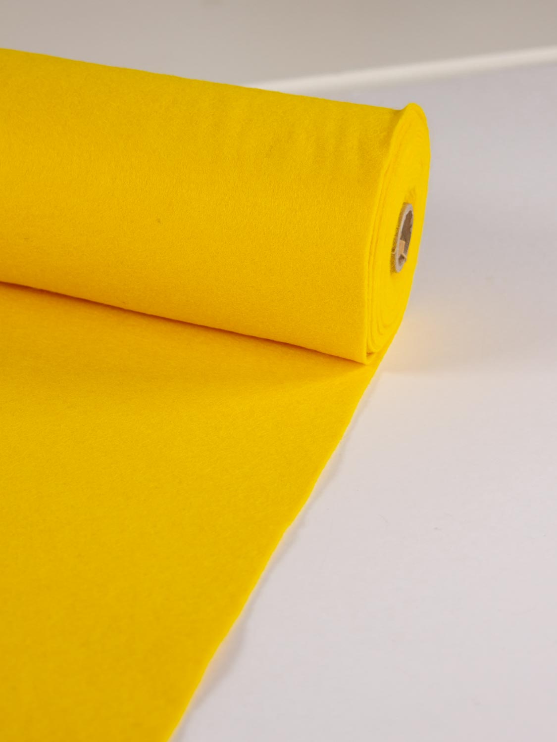 A roll of warm yellow wool and viscose felt fabric unrolled out onto a clean white surface.