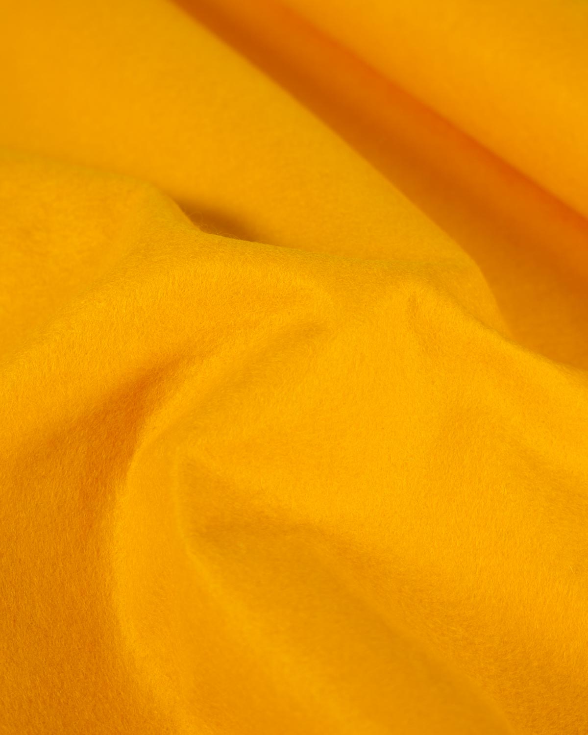 A gathered piece of fiesta yellow wool and viscose felted fabric, showing its firm structure and texture and bold, bright colour.