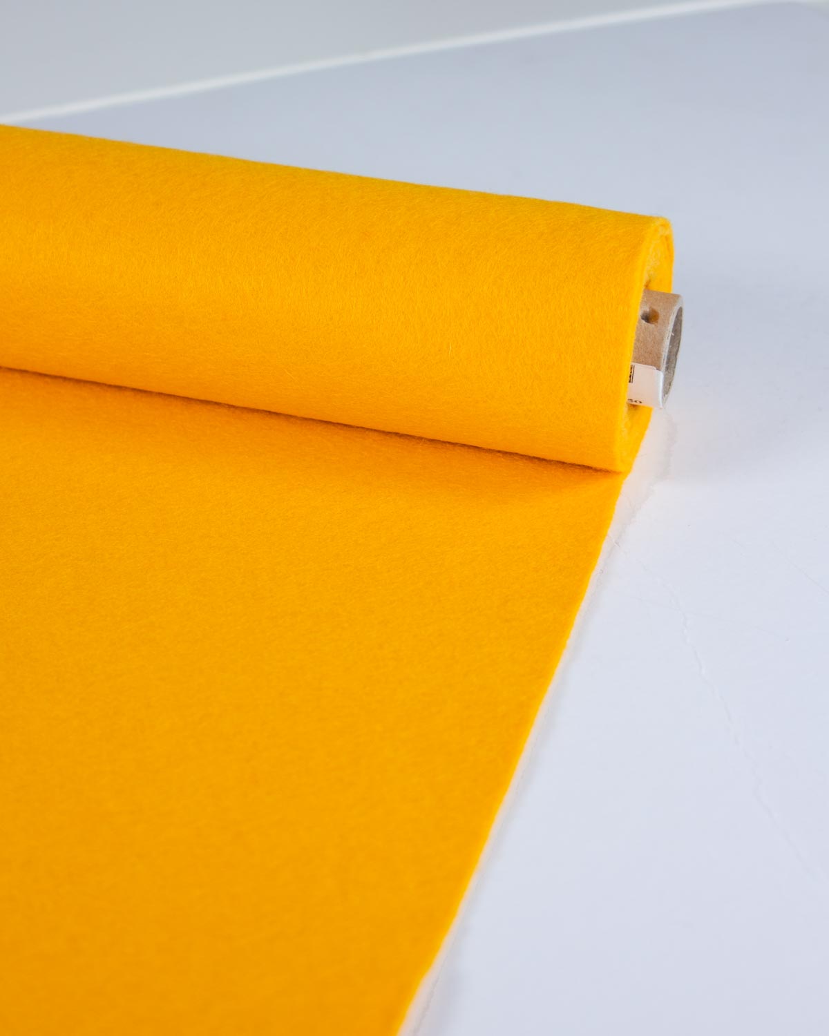 A roll of bright fiesta yellow wool and viscose felt fabric partially unrolled on a clean white surface, showcasing its bold and even colour. 