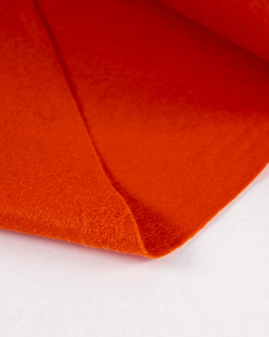 A close-up of bright orange wool and viscose felt fabric folded over itself on a plain white background.