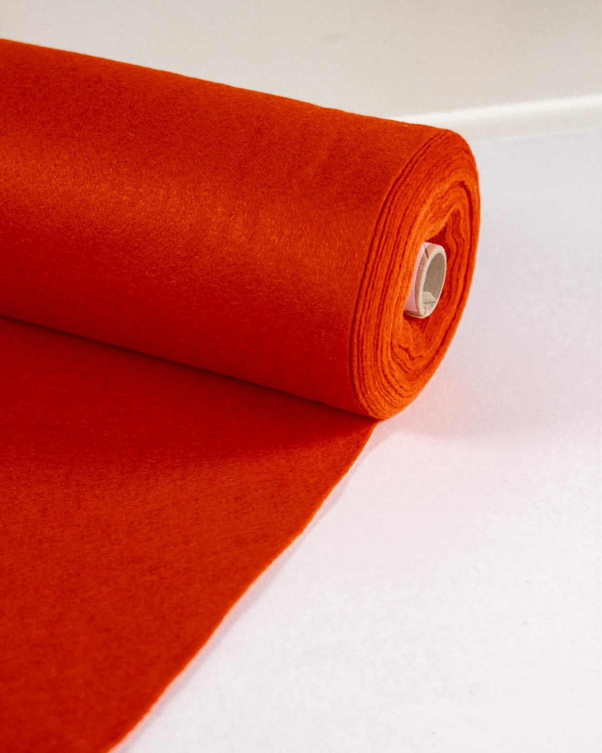 A roll of bright orange wool and viscose felt fabric unrolled, set against a clean white background.