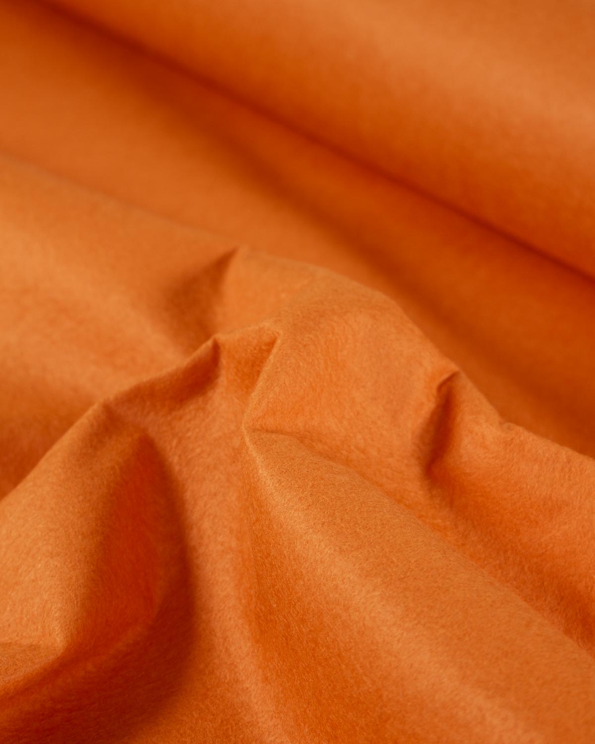 A close-up of draped light orange fabric with soft folds and a smooth, slightly matte texture.