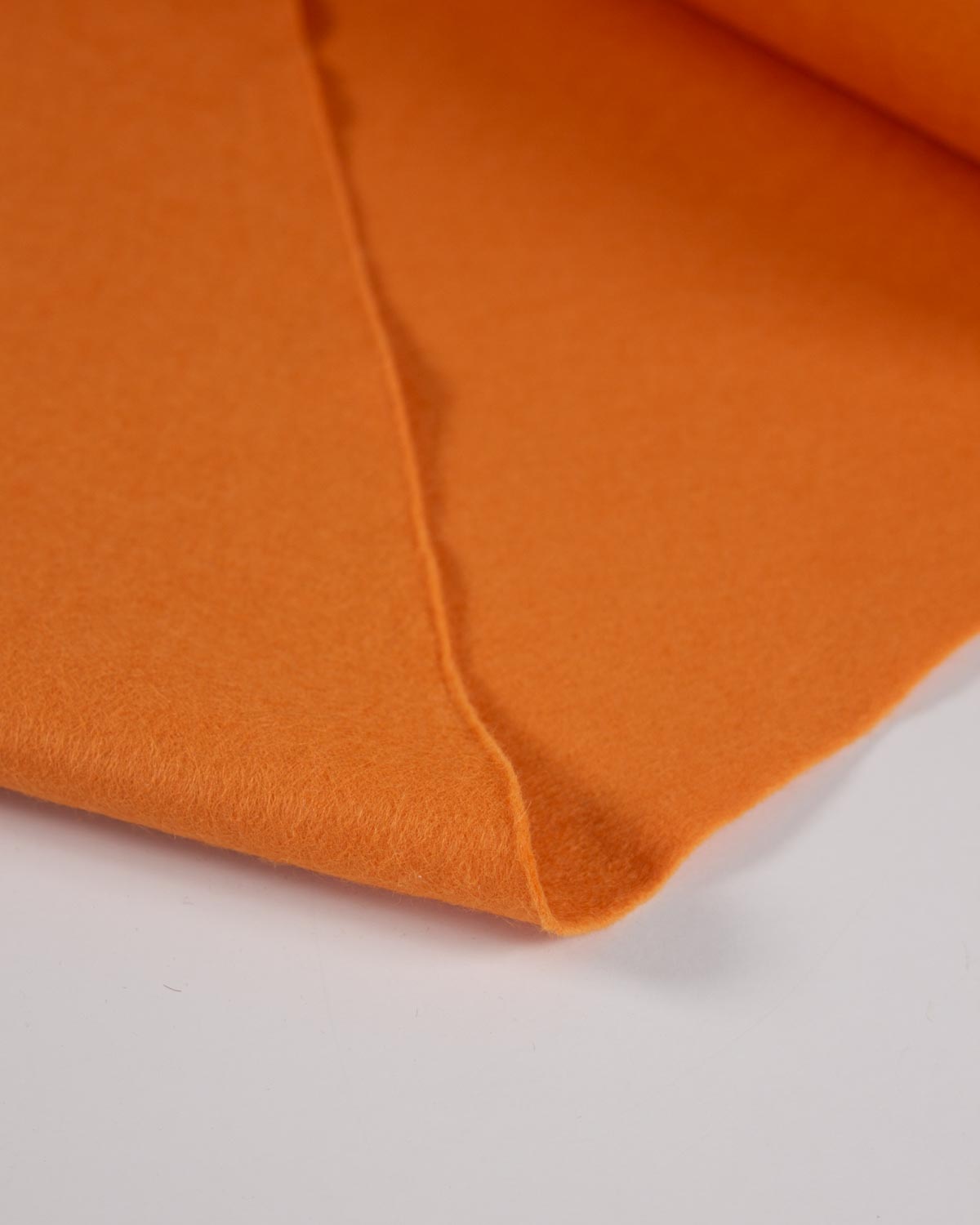 A piece of light warm orange wool and viscose felt fabric folded on a white surface, showing its texture and bold colour. 