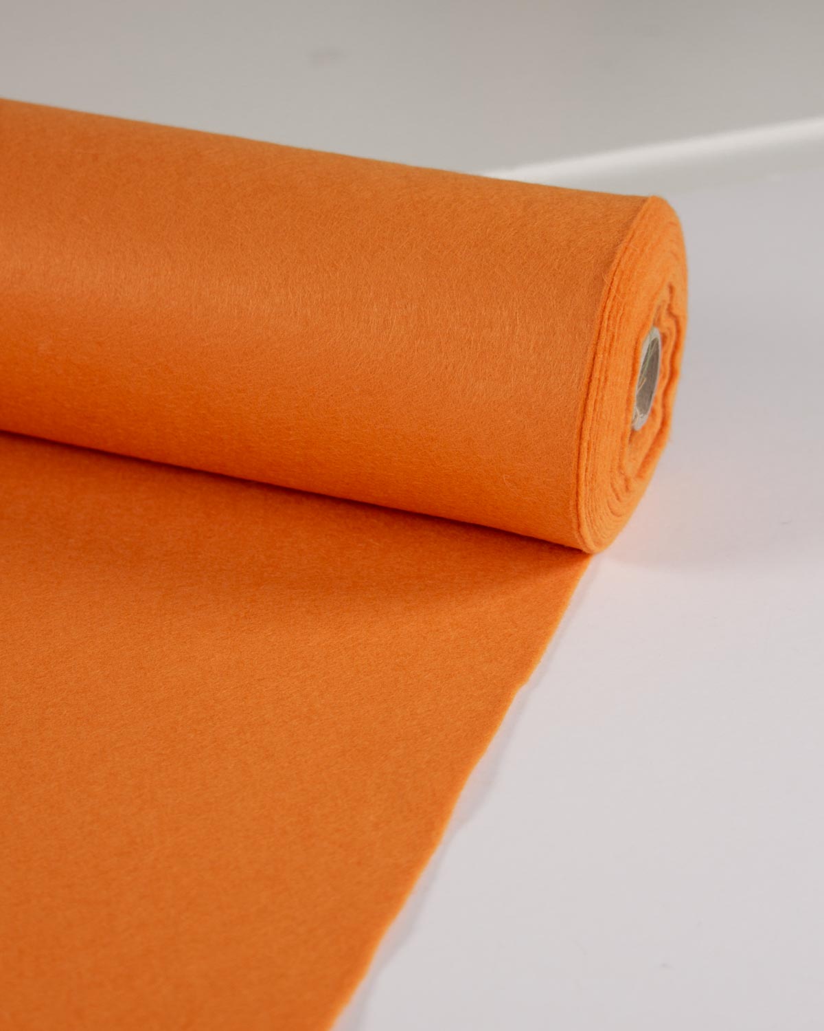 A roll of bright orange wool and viscose felt fabric partially unrolled on a clean white surface.