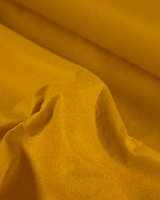 A scrunched up piece of gold-yellow wool and viscose felt fabric, showing off its bold colour and textured surface. 
