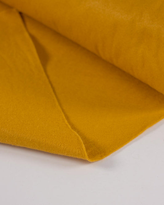 A piece of gold-yellow wool and viscose felt fabric folded on a white background, showing its even colour and textured surface.