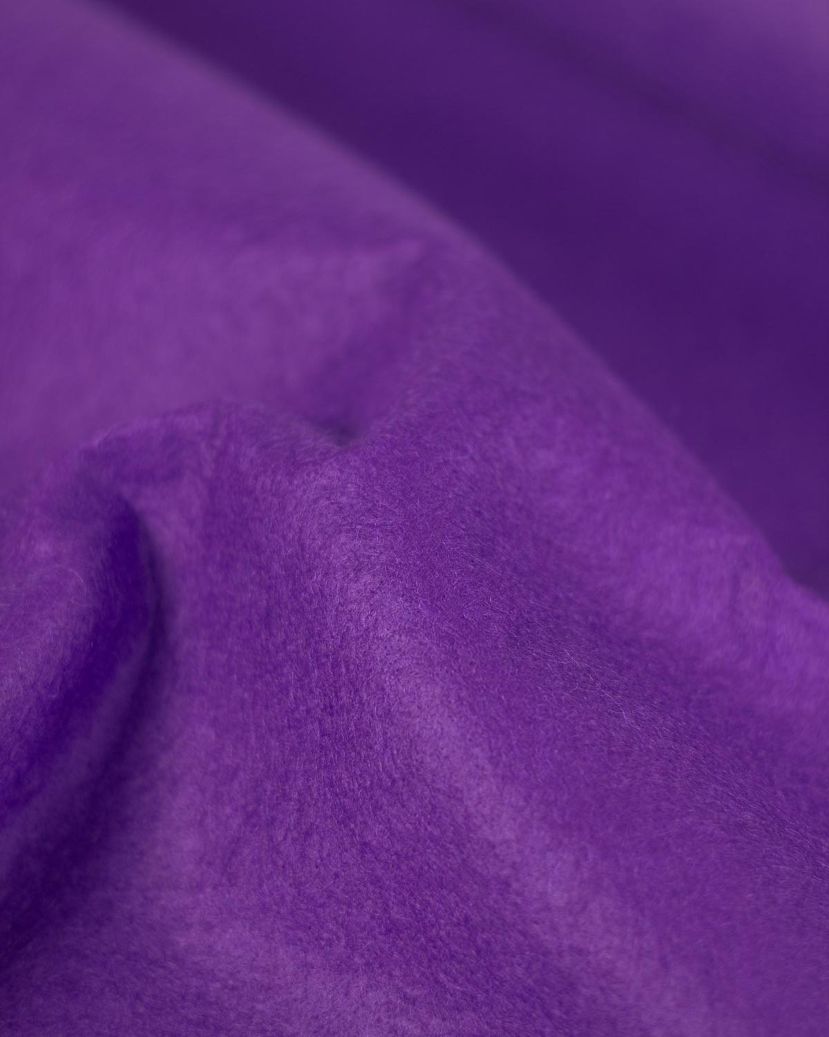 Purple wool and viscose felt fabric, gathered up to show its firm structure and textured surface. 