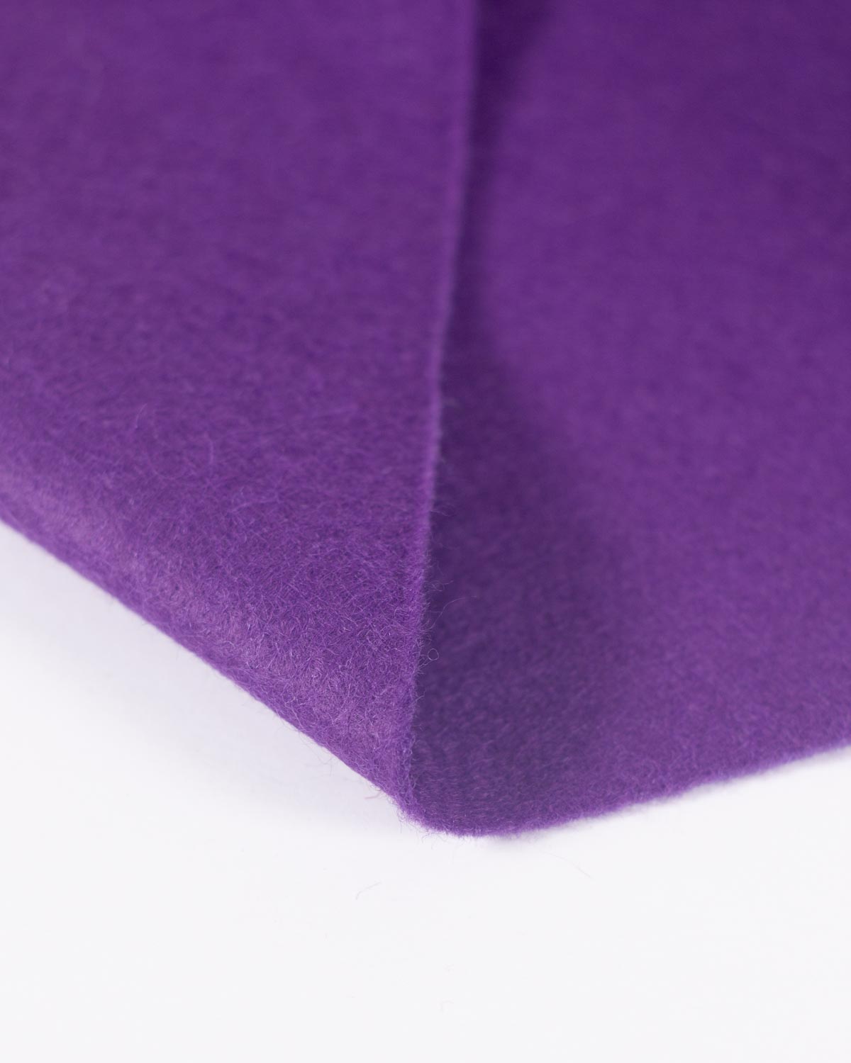 A piece of purple wool and viscose felt fabric, folded on a white background, showcasing its texture as well as a bold and even colour. 