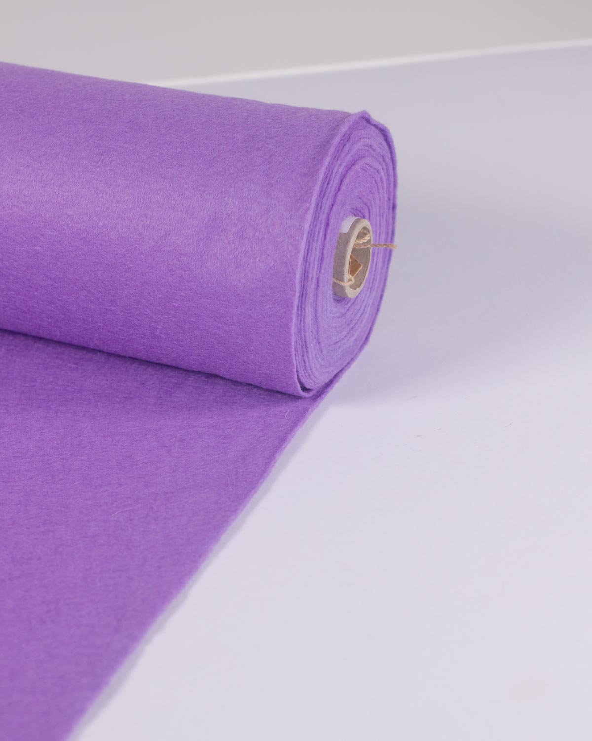 A roll of lilac purple wool and viscose felt fabric, partially unrolled onto a plain white background showing its bold, even colour.