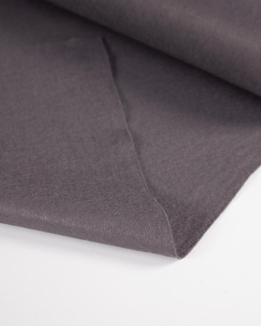 A close-up of folded dark grey wool and felt fabric showing its soft texture and matte finish on a clean white background.