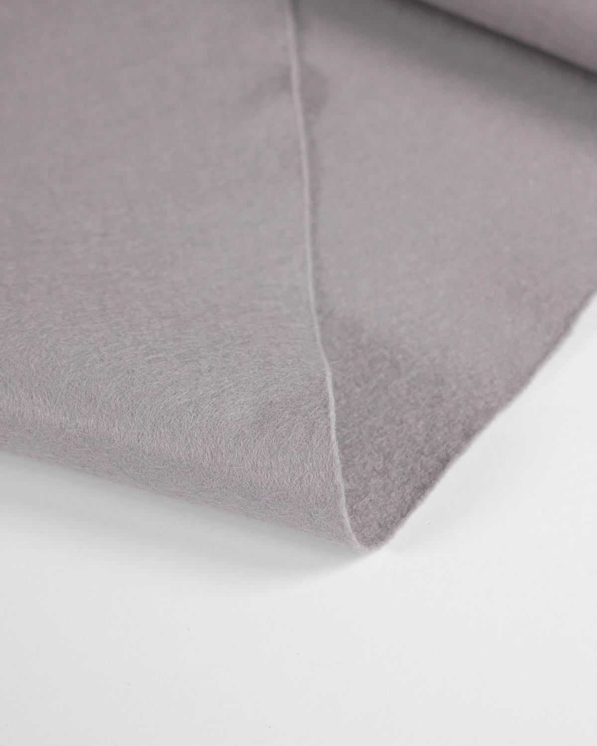 A close-up of a folded piece of light grey wool and viscose felt fabric showing its soft texture and clean edge against a white background.