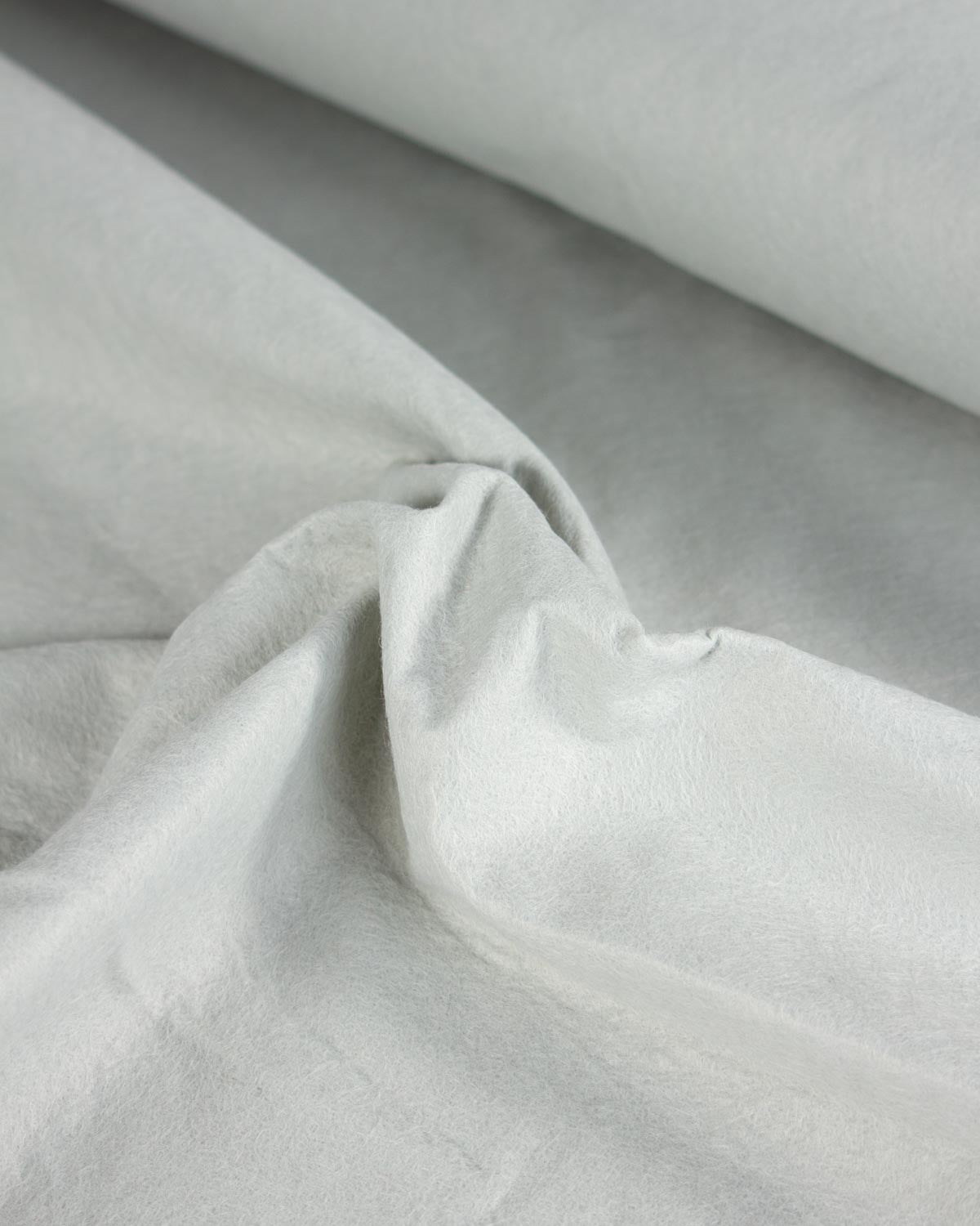 A close-up of light grey wool and viscose felt fabric with soft folds and a rolled section at the top, showing the material texture and color.