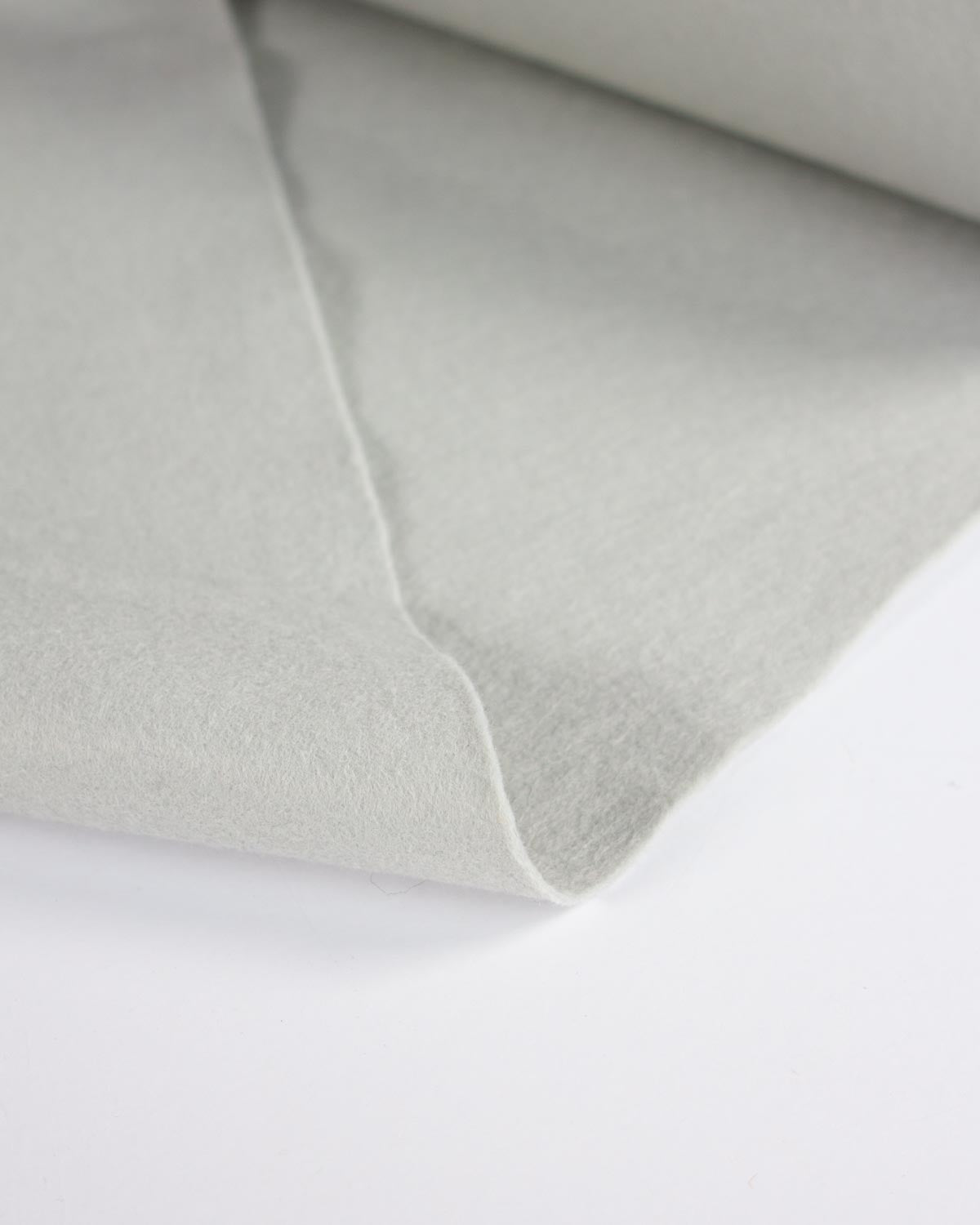 A close-up of a light grey wool and viscose felt fabric, showing its soft texture and folded edges against a plain white background.