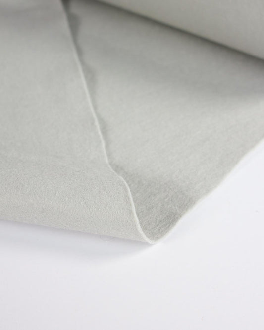 A close-up of a light grey wool and viscose felt fabric, showing its soft texture and folded edges against a plain white background.