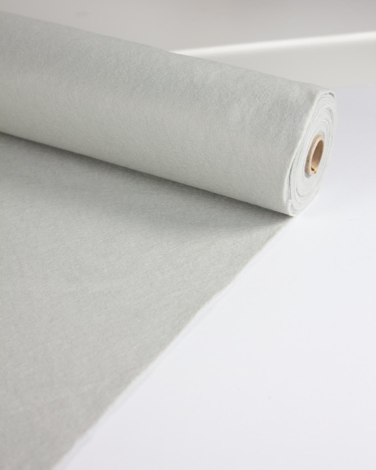 A roll of light grey wool and viscose felt fabric material partially unrolled on a clean white surface.